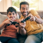 An older and younger brother play video games together at home. 